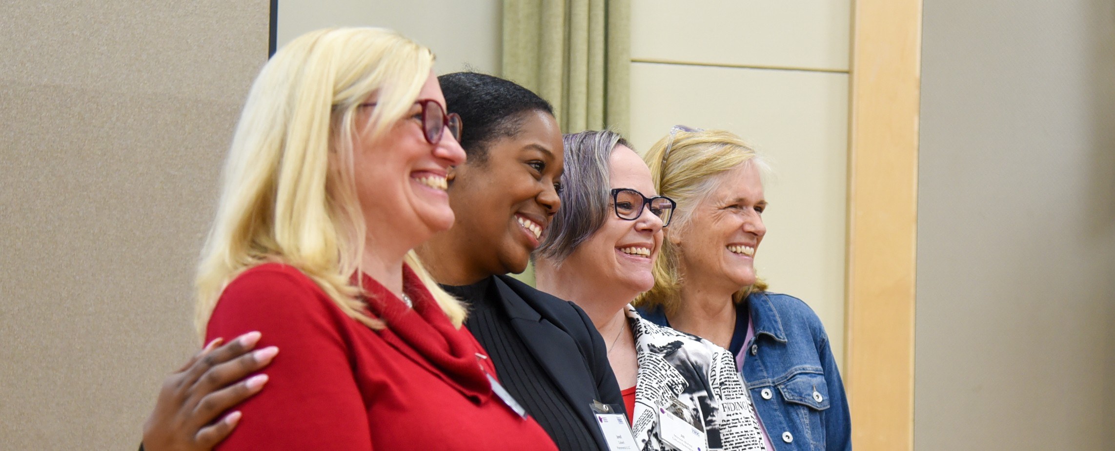 4 women standing together look to the right and smiling at the camera