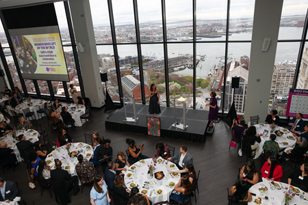 people seated at tables and person speaking at podium